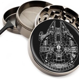 Puede incluir: Un molinillo de metal con una base negra y un contorno blanco de la nave espacial Millennium Falcon. El molinillo tiene una tapa extra&iacute;ble, una pantalla y un raspador.