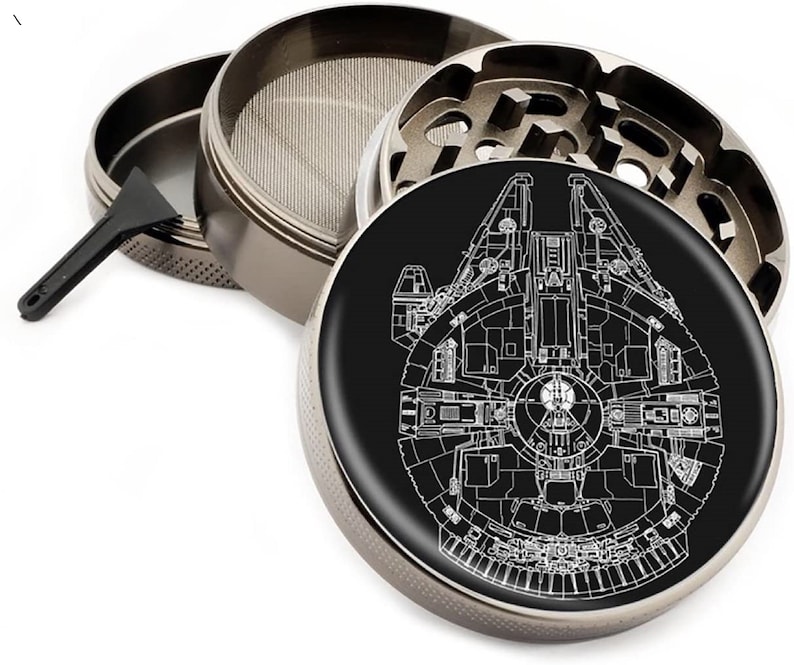 Puede incluir: Un molinillo de metal con una base negra y un contorno blanco de la nave espacial Millennium Falcon. El molinillo tiene una tapa extra&iacute;ble, una pantalla y un raspador.