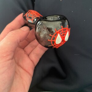 May include: A black glass smoking pipe with a red and white spider web design.