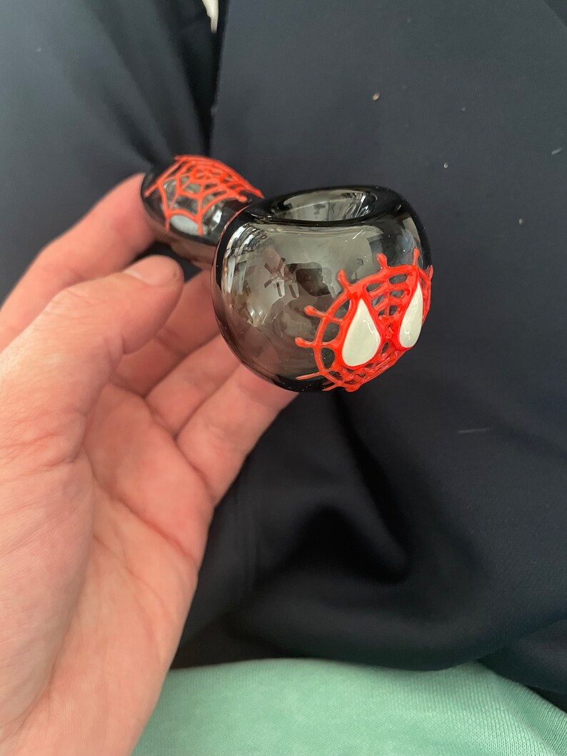 May include: A black glass smoking pipe with a red and white spider web design.