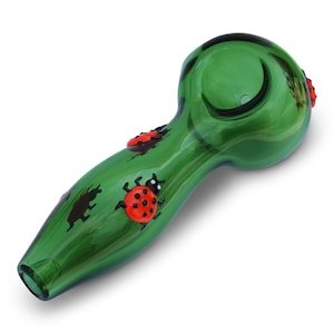 May include: Green glass smoking pipe with ladybug designs. The pipe has a bowl on one end and a mouthpiece on the other.