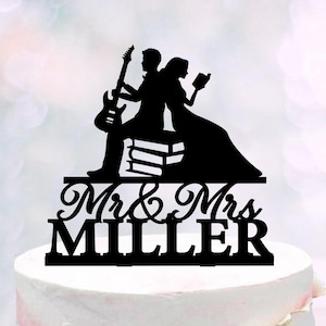 Può includere: Topper per torta in silhouette nera di una coppia, una donna che legge un libro e un uomo che suona la chitarra, in piedi su una pila di libri. Il testo "Mr. & Mrs. Miller" è sotto la coppia.