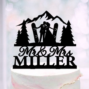 May include: Black silhouette of a couple kissing in front of a mountain range with two ski silhouettes. The text "Mr. & Mrs. Miller" is below the couple.
