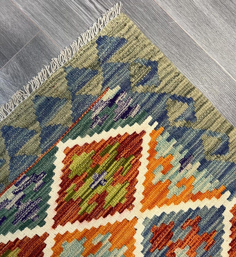 May include: A colorful rug with a geometric pattern in shades of blue, green, orange, and brown. The rug has a fringe border.