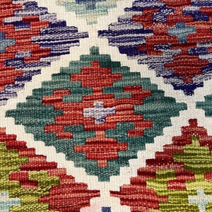 May include: A close-up of a colorful woven rug with a geometric pattern. The rug features shades of red, green, blue, and white.