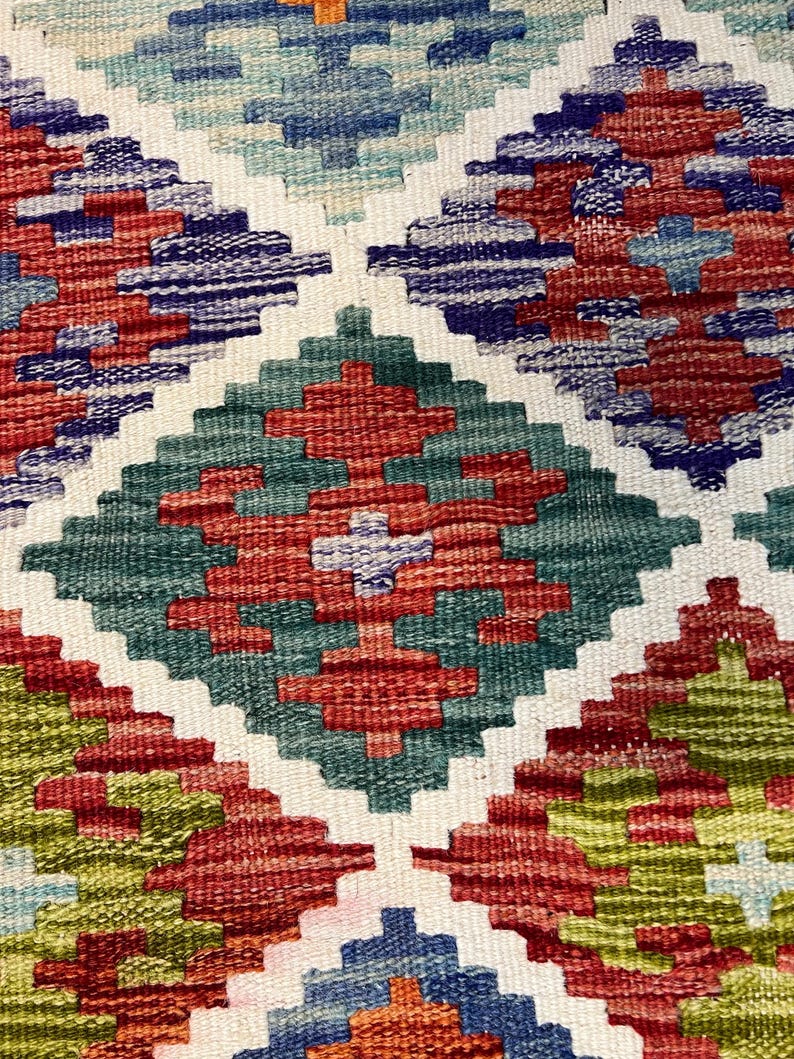 May include: A close-up of a colorful woven rug with a geometric pattern. The rug features shades of red, green, blue, and white.