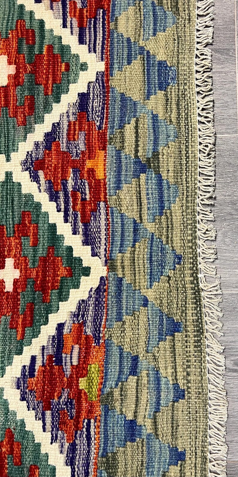 May include: A colorful rug with a geometric pattern in shades of red, blue, green, and white. The rug has a fringe border.