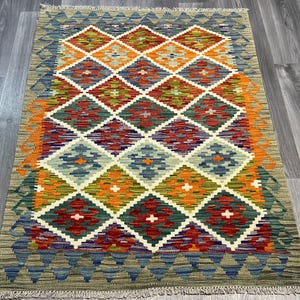 May include: A colorful rug with a diamond pattern in shades of orange, red, green, blue, and white. The rug has a fringe border.