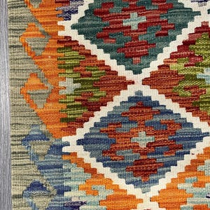 May include: A colorful rug with a geometric pattern in shades of orange, blue, green, and red. The rug has a diamond-shaped design with intricate details.