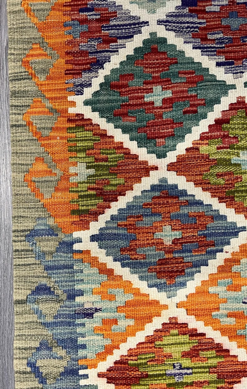 May include: A colorful rug with a geometric pattern in shades of orange, blue, green, and red. The rug has a diamond-shaped design with intricate details.