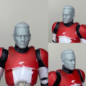 May include: A close-up of a gray plastic action figure head with a short, spiky hairstyle. The figure is wearing a red and white armor with black accents.