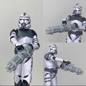 Può includere: Tre action figure di cloni di Star Wars, bianche e grigie, che tengono un'arma blaster grigia a più canne. Le figure sono in pose d'azione diverse.