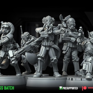 May include: A set of seven grey unpainted miniature figures standing on circular bases. The figures are equipped with various futuristic weapons and tactical gear. The text "THE BAD-ASS BATCH" is visible in the top left corner, with "WAR BEAR STUDIOS" and "THE BAD-ASS BATCH" at the bottom left.