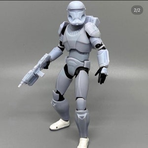 Puede incluir: Una figura de acción de plástico blanco de un soldado que lleva un casco y una armadura, sosteniendo un arma. La figura está en posición de pie con una pierna hacia adelante y la otra hacia atrás. La figura lleva un casco blanco con una visera negra. La figura lleva una armadura blanca con detalles negros. La figura sostiene un arma blanca con un mango negro.