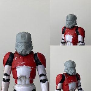 Può includere: Un casco di plastica grigio con una placca toracica e spalline rosse e bianche. Il casco ha una visiera e un design dettagliato.