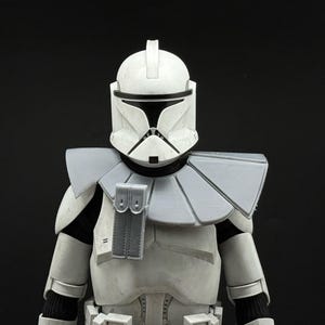 May include: A detailed, close-up view of a white and gray Clone Trooper helmet and armor. The helmet has a distinctive T-shaped visor and a vertical fin on top. The armor includes shoulder pauldrons and a chest plate, all in shades of white and gray.