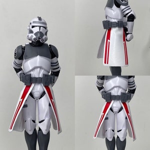 Könnte beinhalten: Eine weiße und graue Actionfigur eines Star Wars Klonkriegers, der einen weißen und roten Umhang trägt. Die Figur hat einen Helm mit einem grauen Visier und eine schwarze und graue Brustplatte.