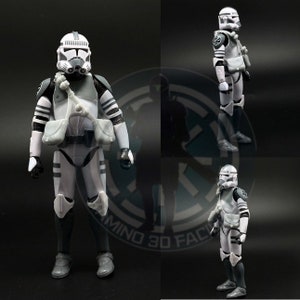 May include: A white and gray action figure of a Star Wars clone trooper. The figure is wearing a white helmet with a black visor, a white and gray armor, and a black and gray backpack. The figure is standing on a black surface.