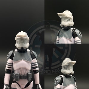 May include: A white and grey action figure of a Star Wars clone trooper with a helmet. The helmet has a visor and a large, flat top. The figure is wearing a white and grey armour with a black belt. The figure is standing on a black surface.
