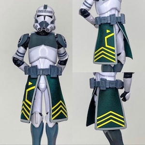 May include: A Star Wars Clone Trooper action figure in white, gray, and dark green armor. The figure has a helmet, chest armor, and a dark green skirt with yellow chevron designs. A gray belt is around the waist.