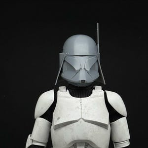 May include: A gray and white costume resembling a helmet and armor. The helmet has a distinctive shape with a vertical antenna. The armor is white with black accents and appears to be made of hard plastic. The costume is set against a black background.