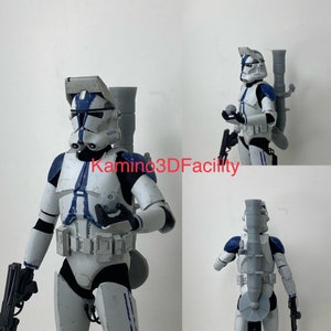 Puede incluir: Una figura de acción de un clon de soldado de Star Wars blanco y azul con una mochila y un rifle bláster. La figura sostiene un pequeño objeto redondo en su mano izquierda. La figura está en posición de pie con la pierna derecha ligeramente hacia adelante.
