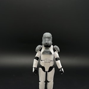 May include: A white and gray action figure of a character in a futuristic suit, with a helmet and armor. The figure is standing against a dark background, showcasing the details of the costume.