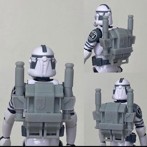 Op de afbeelding: Een wit en grijs actiefiguur van een soldaat met een helm en een grijze rugzak. Het figuur heeft grijze accenten op de helm en armen. De rugzak heeft twee cilindrische opzetstukken en een rechthoekige centrale component.