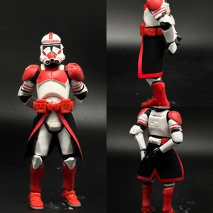 May include: A red and white Star Wars action figure with a black cape. The figure is wearing a helmet and has a red and white design on its armor. The figure is standing on a black surface.