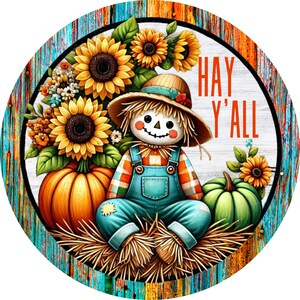 May include: A round wooden sign with a blue and orange distressed wood background. A scarecrow with a straw hat sits in the center of the sign, surrounded by sunflowers and pumpkins. The sign says "Hay Y'all" in orange letters.