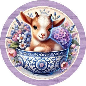 May include: A cute brown and white baby goat sitting in a blue and white porcelain teacup with pink, purple, and blue flowers around it.