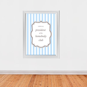Peut inclure: Un cadre accroché à un mur blanc avec un sol en bois. L'impression présente un fond à rayures bleu clair et blanc avec un cadre décoratif contenant le texte "OFFICIEL président du homebody club."