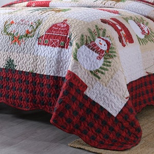 May include: A red and white patchwork quilt with a Christmas theme. The quilt features a snowman, a barn, and a wreath. The quilt has a red and black checkered border.