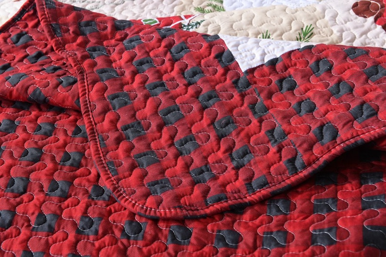 May include: Red and black plaid quilt with a quilted pattern of small circles. The quilt is folded over itself, showing the stitching detail.
