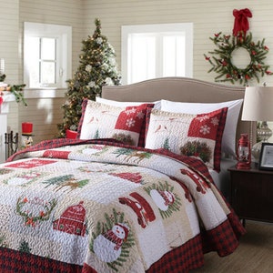 May include: A red and white Christmas themed quilt set with a snowman, a red truck, and a barn. The quilt is made of a soft, quilted fabric and features a patchwork design.