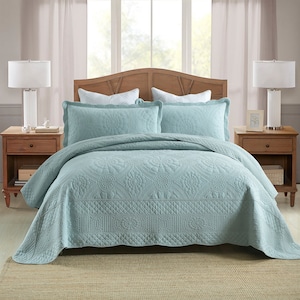 K&ouml;nnte beinhalten: Eine hellblaue gesteppte Bettdecke mit Blumenmuster. Die Bettdecke liegt auf einem Bett mit zwei wei&szlig;en Kissen und einem Kopfteil aus Holz.