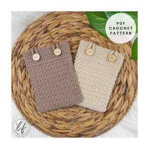 May include: Two crocheted phone cases in beige and taupe, each secured with a wooden button closure. The cases are displayed on a woven, circular placemat. The image includes the text "PDF Crochet Pattern".
