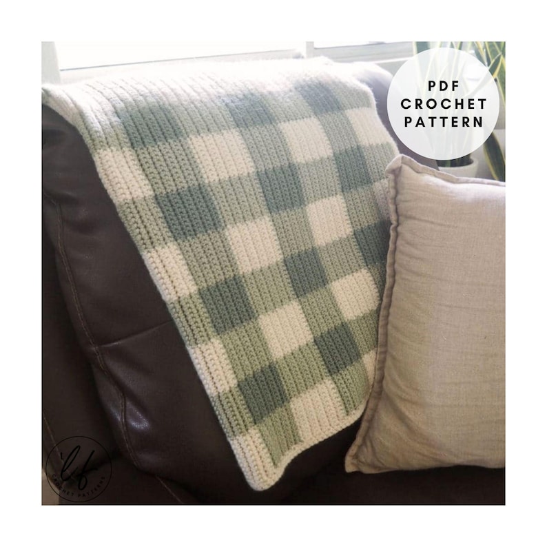 This image shows the sample of this gingham crochet baby blanket pattern laid over the back of an arm chair with a pillow and a plant in the background.