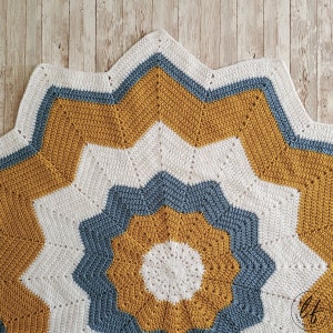 A crocheted star-shaped baby blanket with a white, mustard yellow, and blue color scheme.