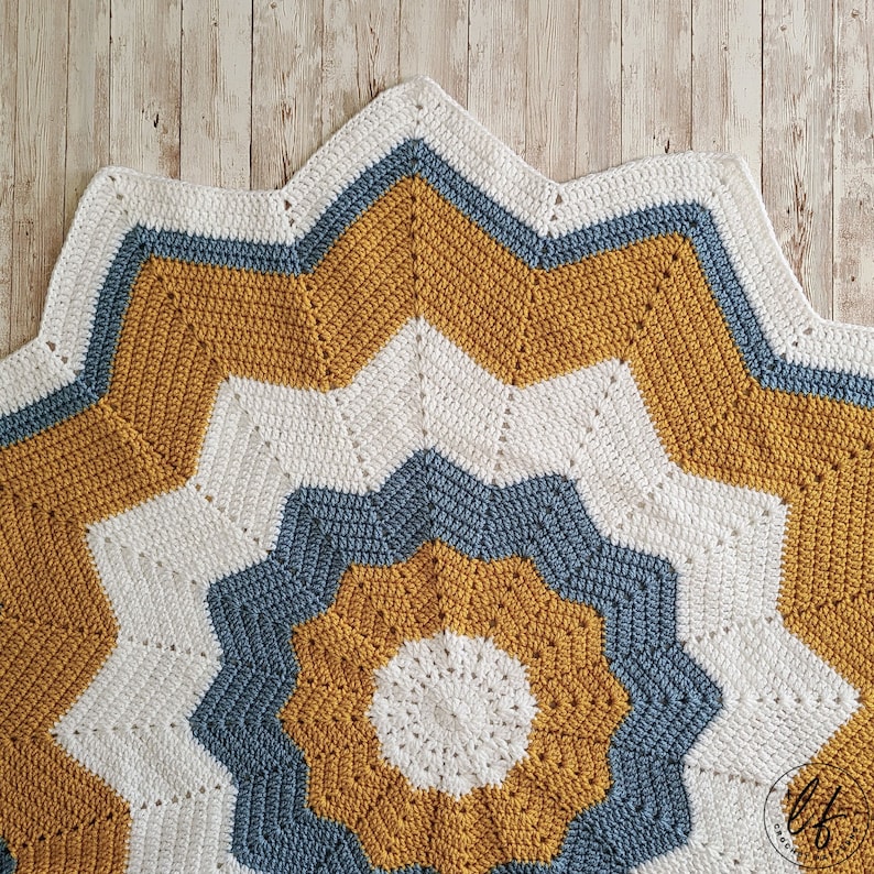 A crocheted star-shaped baby blanket with a white, mustard yellow, and blue color scheme.