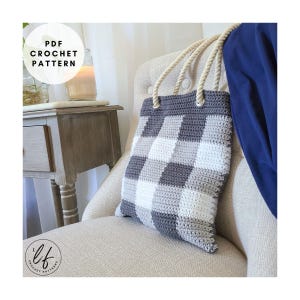 Könnte beinhalten: Gehäkelte Tragetasche mit grau-weißem Karomuster und Seilgriffen. Die Tasche liegt auf einem neutralfarbenen Stuhl. Der Text "PDF CROCHET PATTERN" ist in einem kreisförmigen Grafikdesign zu sehen.