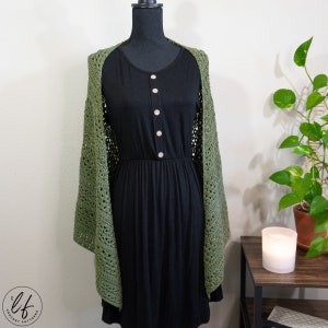 This image shows the crochet triangle shawl pattern sample draped over a mannequin as a women would wear it. The crochet shawl is shown from the front, so the shawl is open and draped over the shoulders. The crochet wrap is made in olive green yarn.