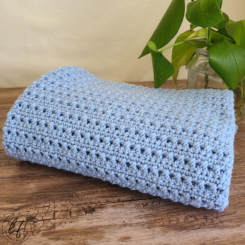 This image shows the finished crochet baby blanket pattern folded up and set on a table with a plant in the background.