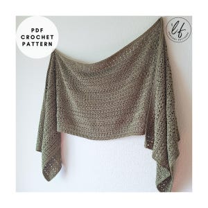Puede incluir: Un chal de ganchillo verde salvia con un patrón texturizado, colgado contra una pared blanca. El chal tiene forma rectangular con detalles calados en los bordes. El texto en la imagen dice "PDF Crochet Pattern".