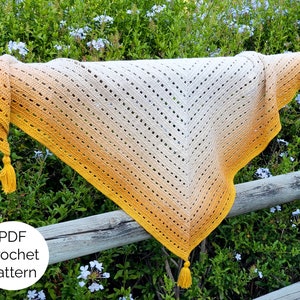 May include: A crochet shawl with a gradient of yellow to white, featuring a delicate openwork stitch pattern. The shawl has tassels on the ends. The text "PDF Crochet Pattern" is visible in the image.