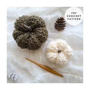 Puede incluir: Dos calabazas hechas a mano con ganchillo, una verde oliva y otra crema, con tallos de ramita. También se ven una piña y un ganchillo de madera. La imagen incluye el texto "PDF Crochet Pattern".