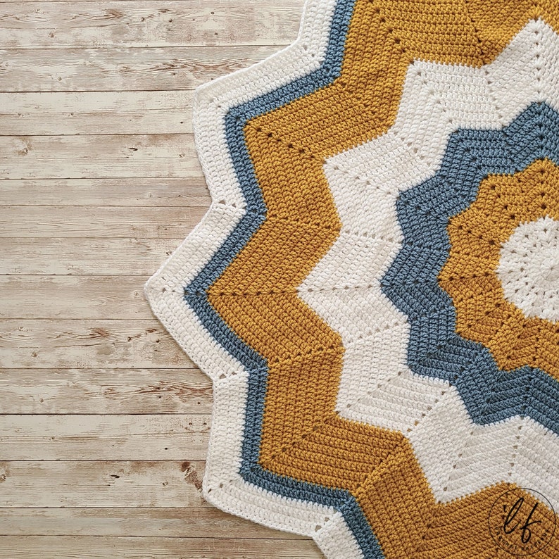 A crocheted 12 point star baby blanket with a white center, surrounded by alternating bands of mustard yellow and blue.