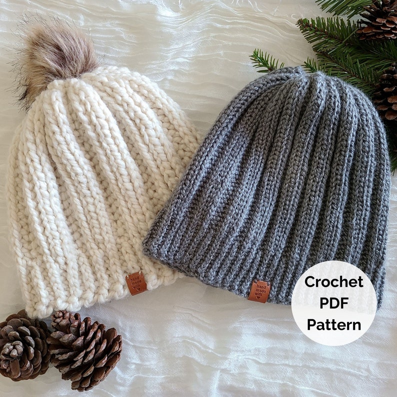 Peut inclure: Deux bonnets crochet&eacute;s faits &agrave; la main, l'un cr&egrave;me avec un pompon en fausse fourrure, l'autre gris. Les deux ont une texture c&ocirc;tel&eacute;e et de petites &eacute;tiquettes en cuir. L'image comprend le texte "Crochet PDF Pattern".