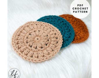 May include: Three handmade crochet coasters in a row. The coasters are circular with a floral design in the centre. Colours include tan, teal, and orange. The image also includes the text "PDF Crochet Pattern".