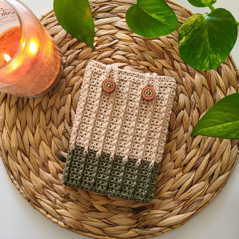 A crochet kindle case with a beige and green color scheme. The case has two wooden buttons with floral designs.